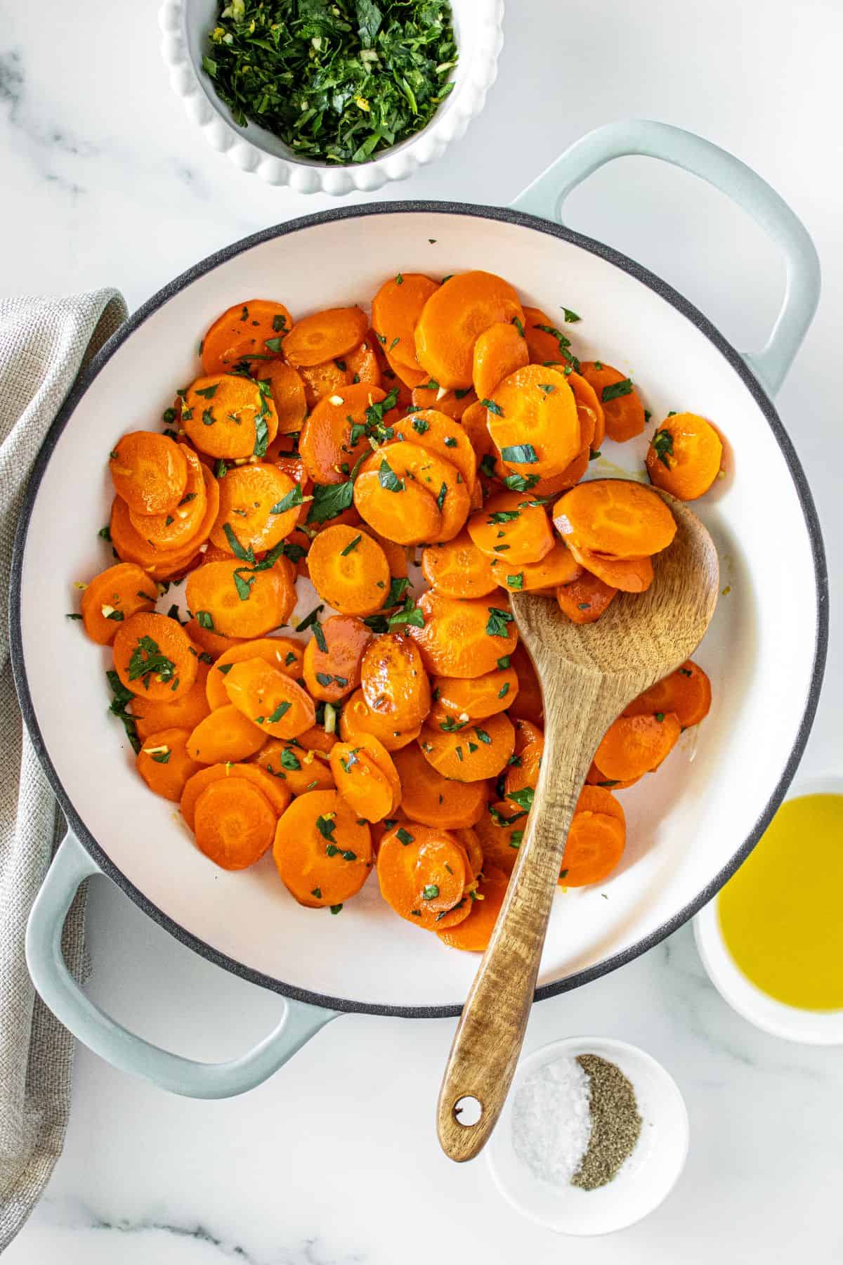 Large frying pan with Sautéed Carrots, topped with gremolata, with a wooden spoon in the pan.