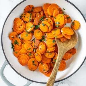 Large frying pan with Sautéed Carrots, topped with gremolata, with a wooden spoon in the pan.