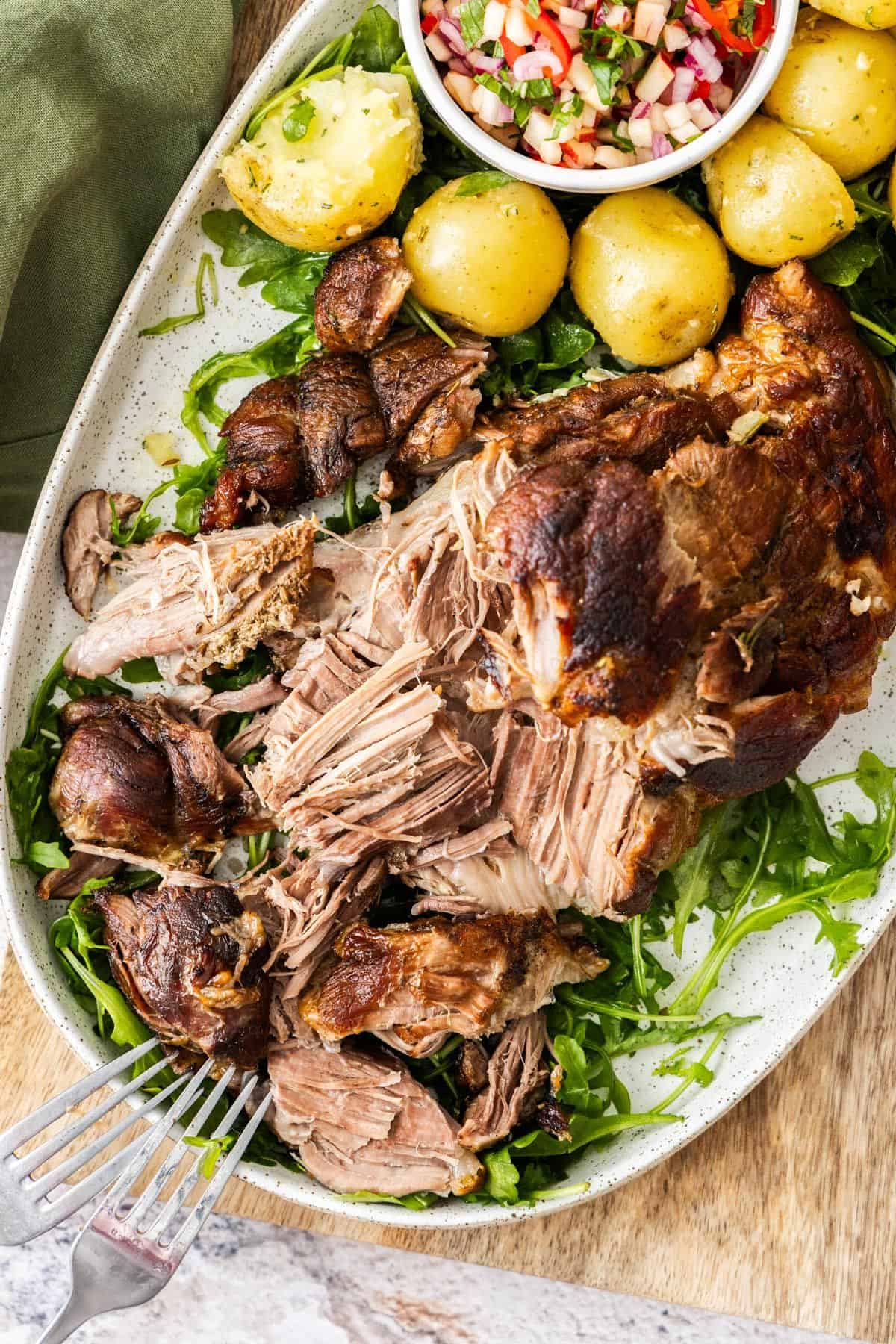 Platter with Slow Roasted Pork Shoulder with some rocket leaves, apple salad and potatoes around the edge.
