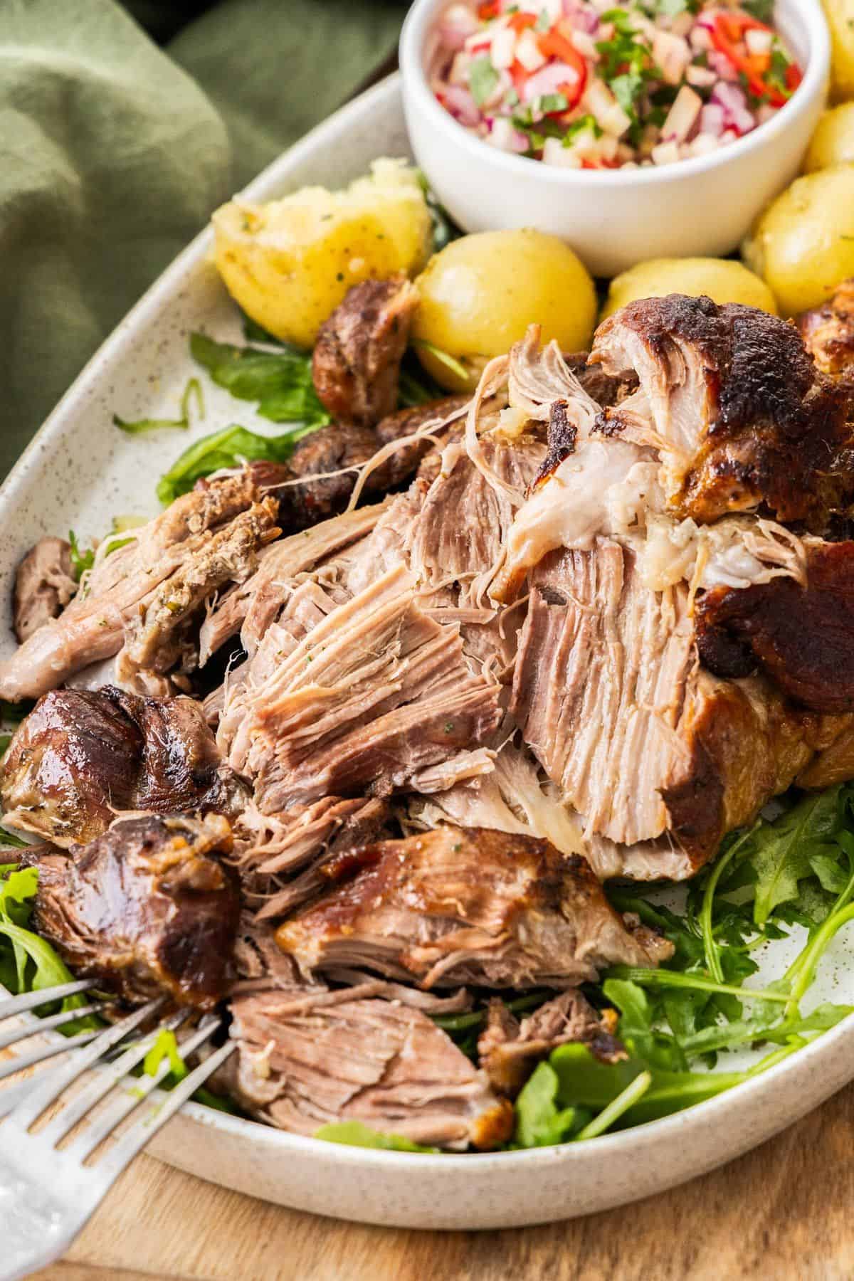 Platter with Slow Roasted Pork Shoulder with some rocket leaves, apple salad and potatoes around the edge.