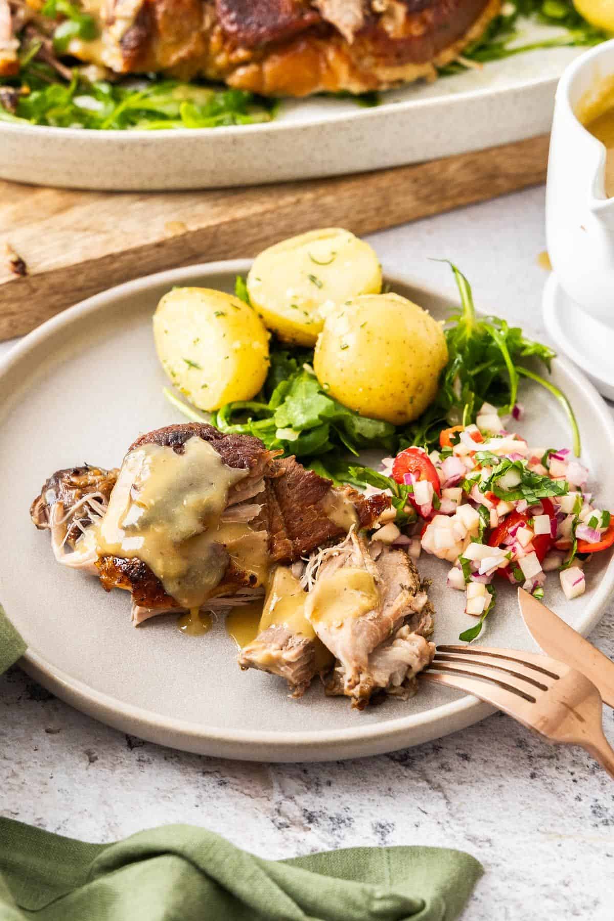 Round grey plate with a serve of Roasted Pork Shoulder, some apple salad, rocket and potatoes.
