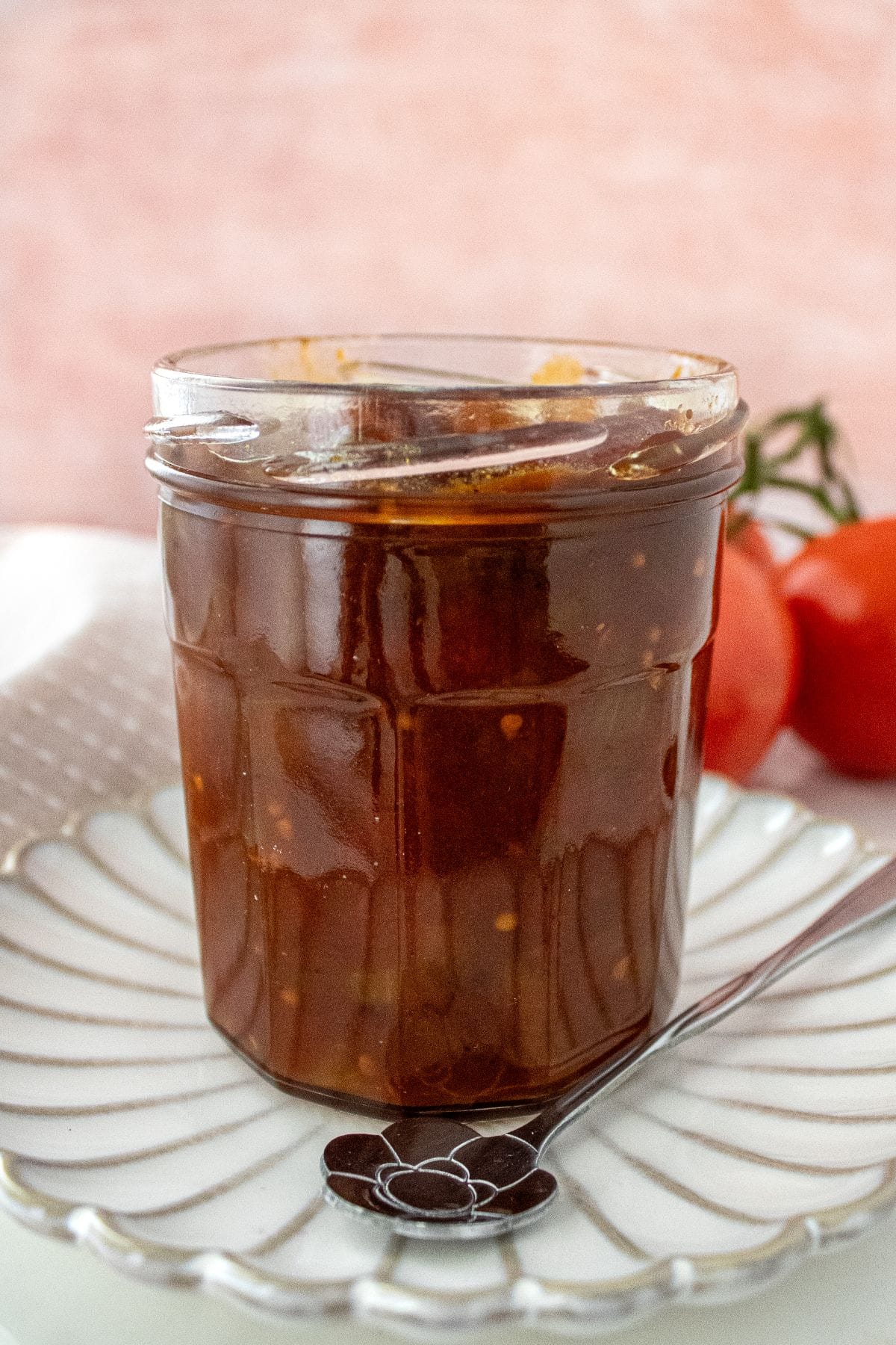 Open jar of Tomato Chutney, on a round white plate, with a spoon on the edge.