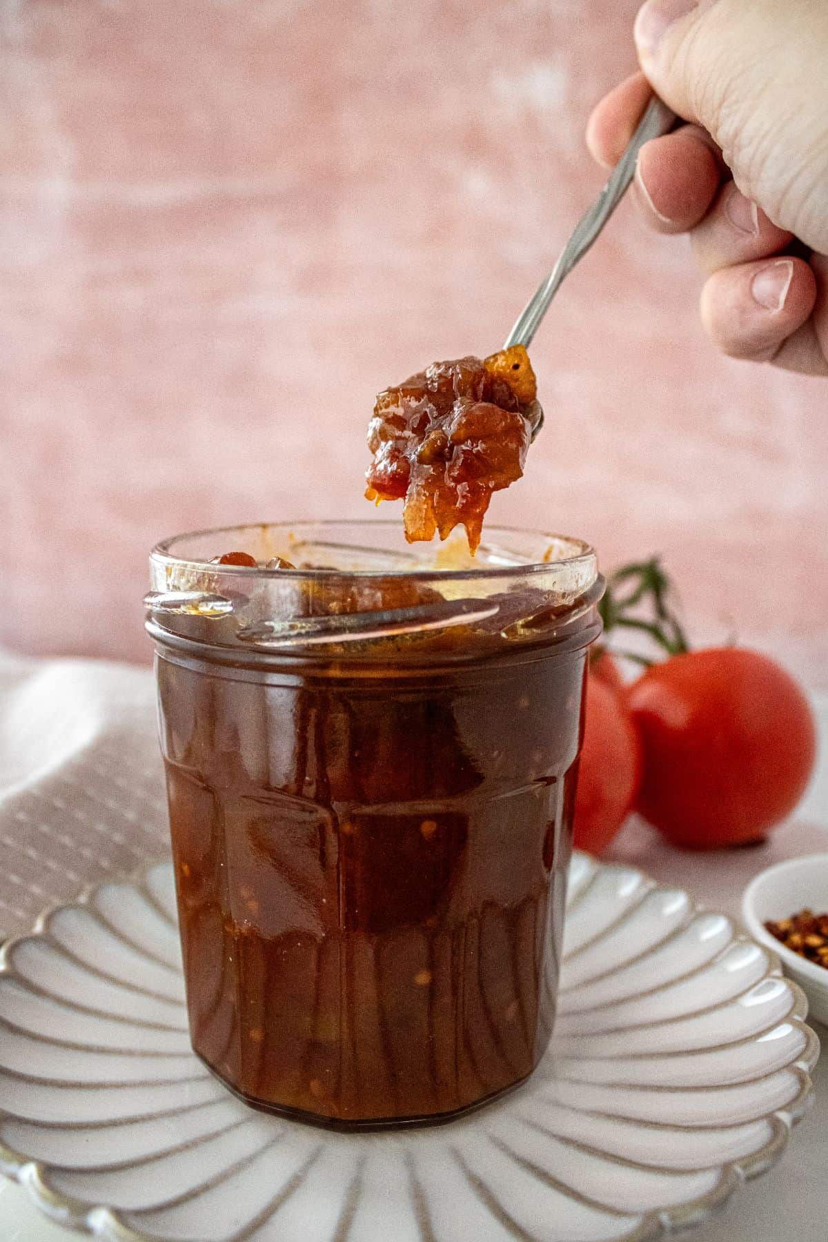 Open jar of Tomato Chutney, on a round white plate, with a spoon scooping up some chutney.