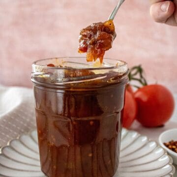 Open jar of Tomato Chutney, on a round white plate, with a spoon scooping up some chutney.