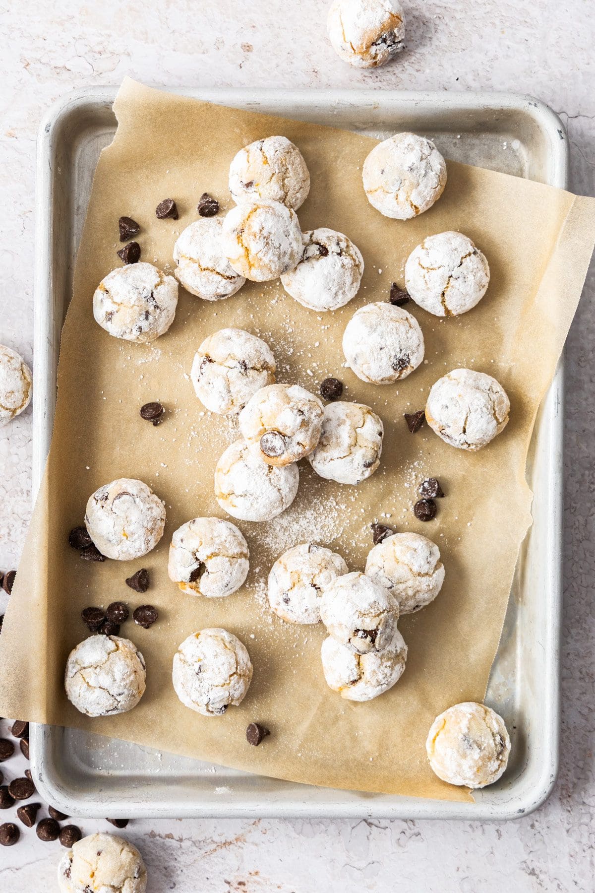 Almond Flour Chocolate Chip Cookies on a baking paper lined tray, with some chocolate chips sprinkled around.