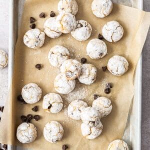 Almond Flour Chocolate Chip Cookies on a baking paper lined tray, with some chocolate chips sprinkled around.