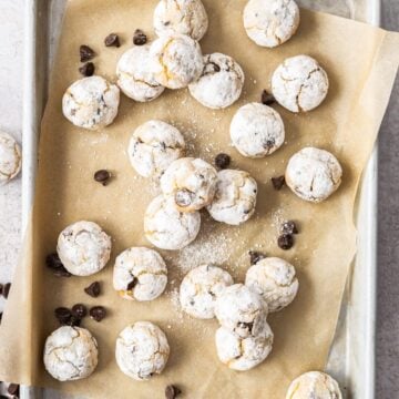 Almond Flour Chocolate Chip Cookies on a baking paper lined tray, with some chocolate chips sprinkled around.