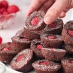 Round white plate with Chocolate Raspberry Bites dusted with icing/powdered sugar, with a hand picking up one of the bites.