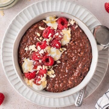 Round bowl of Chocolate Raspberry Porridge topped with yoghurt, flaked almonds and raspberries, with a spoon on the edge.