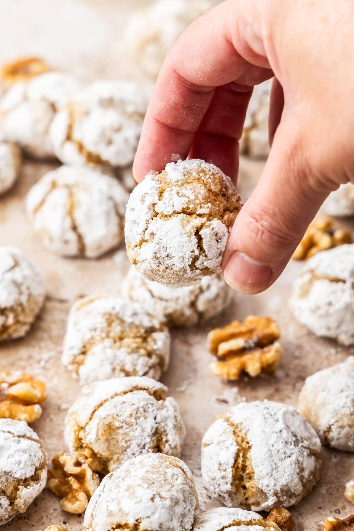 A hand picking up a Walnut Cookie with some more cookies sitting on some baking paper.