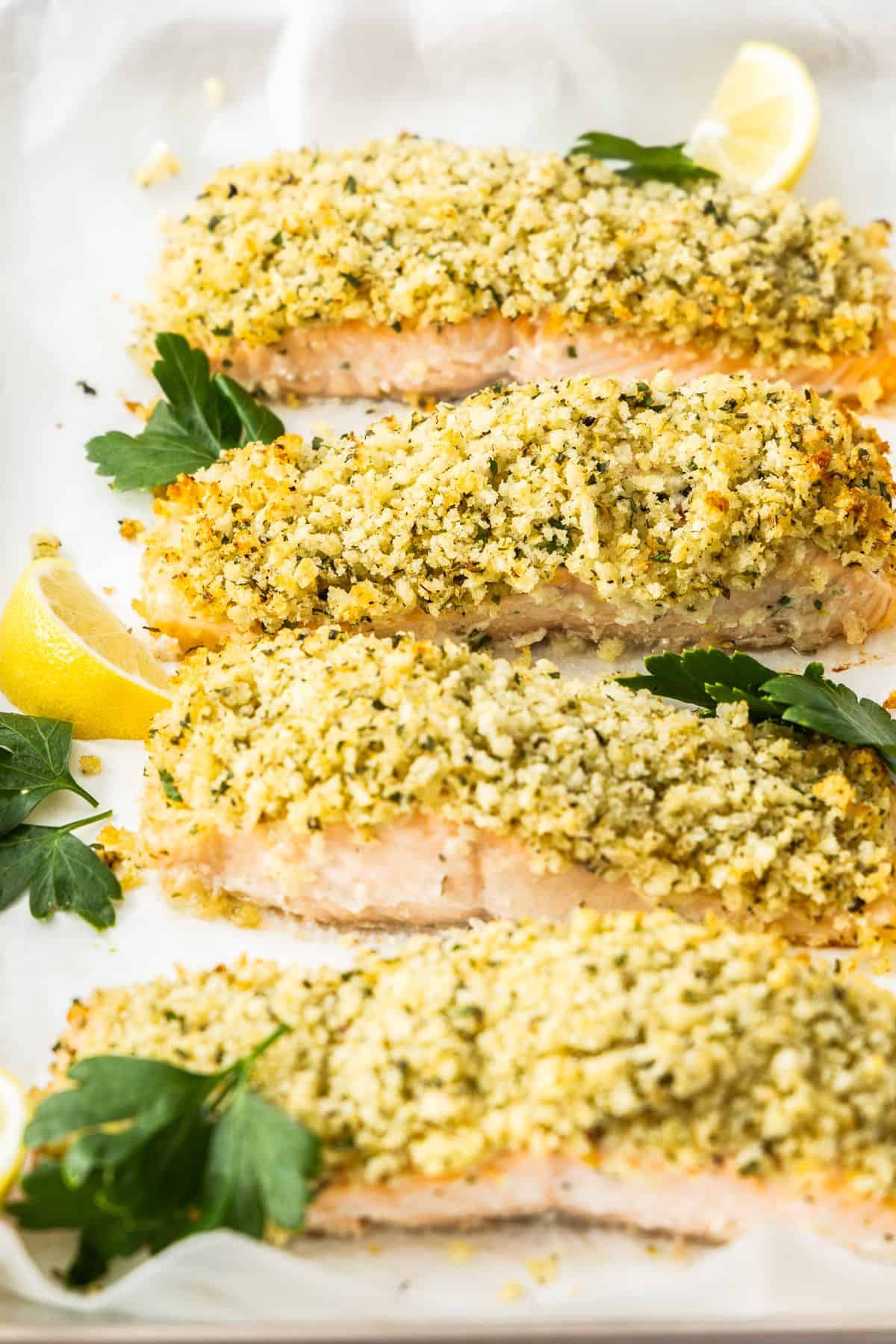Baking tray with cooked Herb Panko Salmon, garnished with some parsley leaves and lemon wedges.
