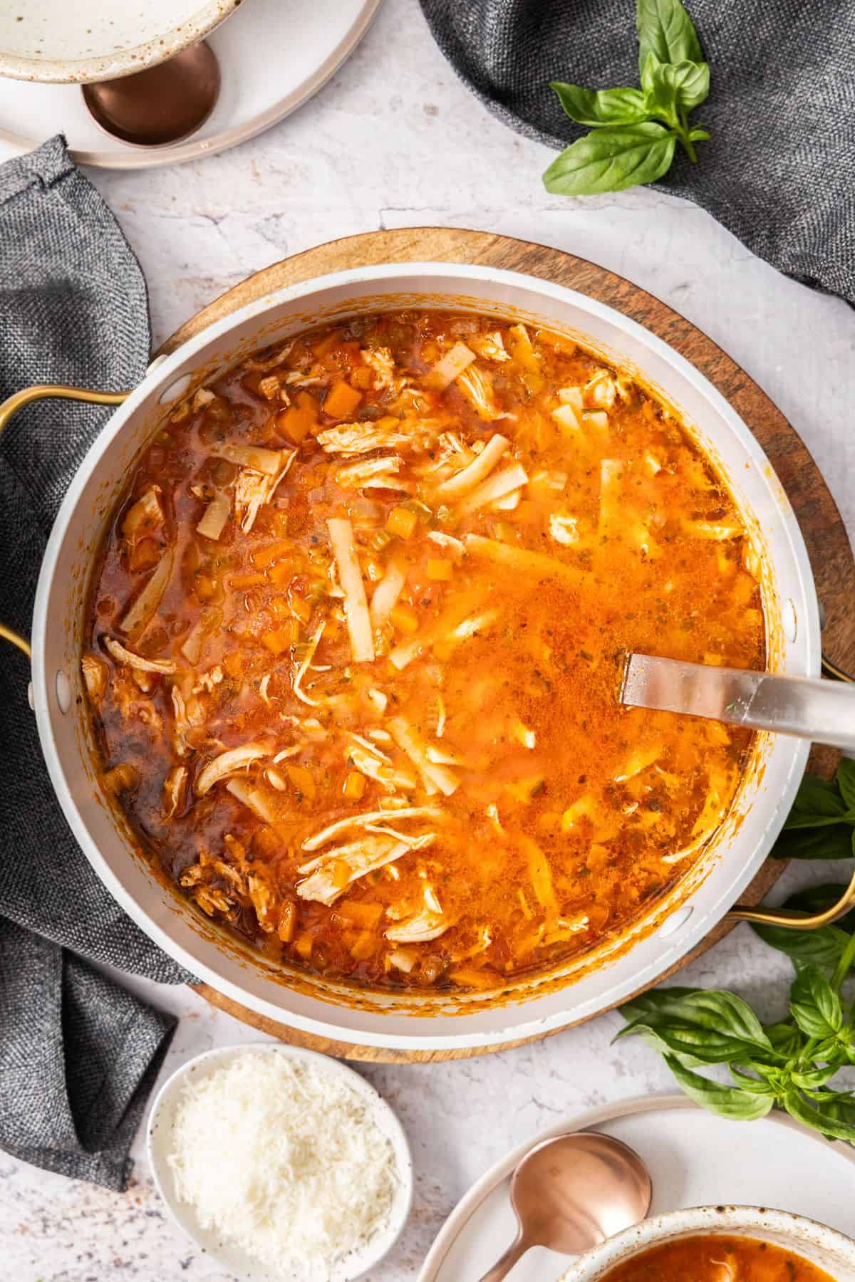 Large saucepan of Mediterranean Chicken Noodle Soup, with a ladle resting in the pan.