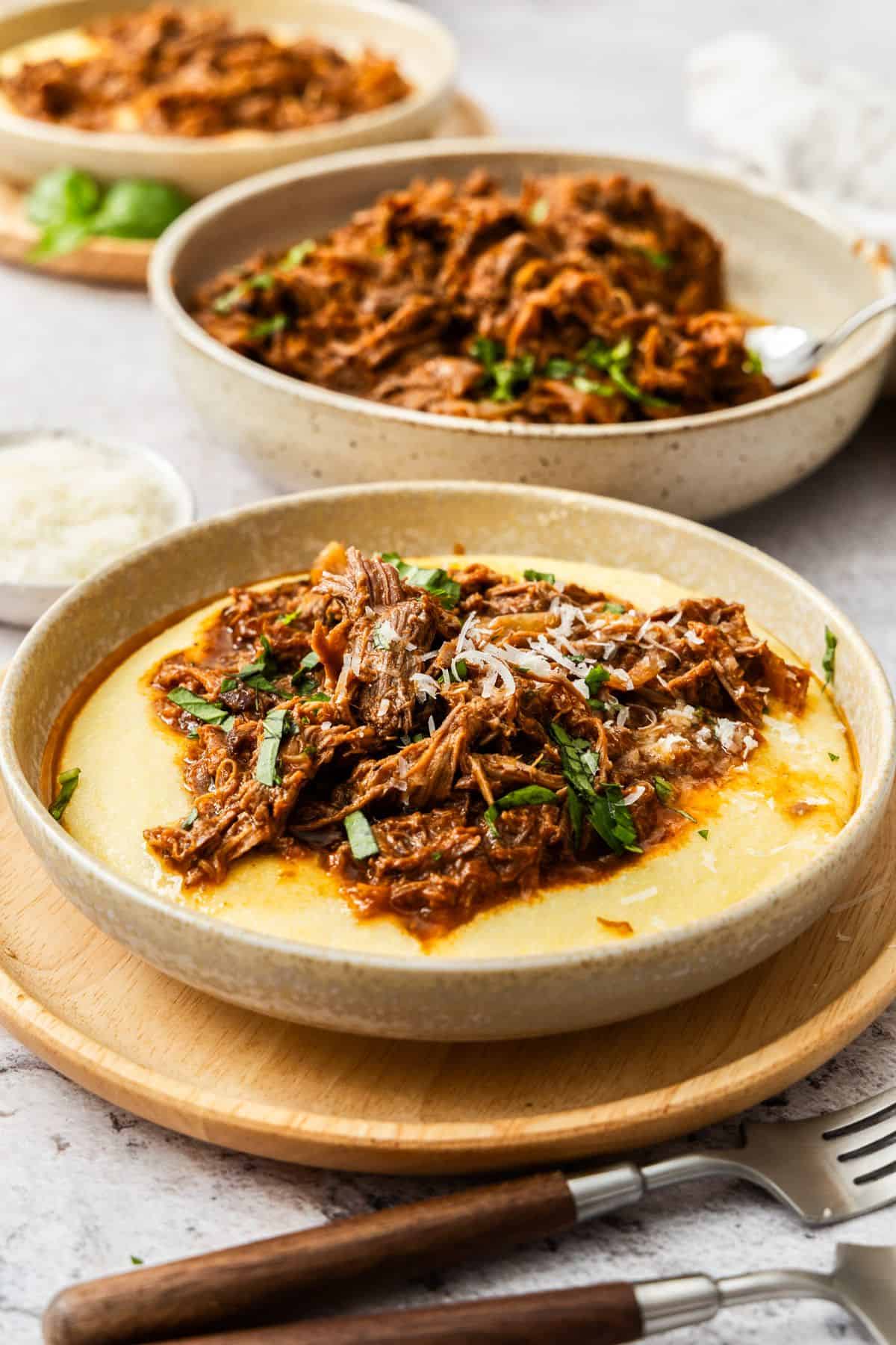 Round dish of Mediterranean Pulled Beef, on a serve of creamy polenta, on a round wooden mat.