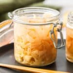 Jar of Pickled Ginger sitting on a black plate, with some chopsticks on edge of plate.