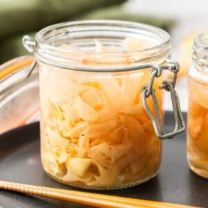 Jar of Pickled Ginger sitting on a black plate, with some chopsticks on edge of plate.