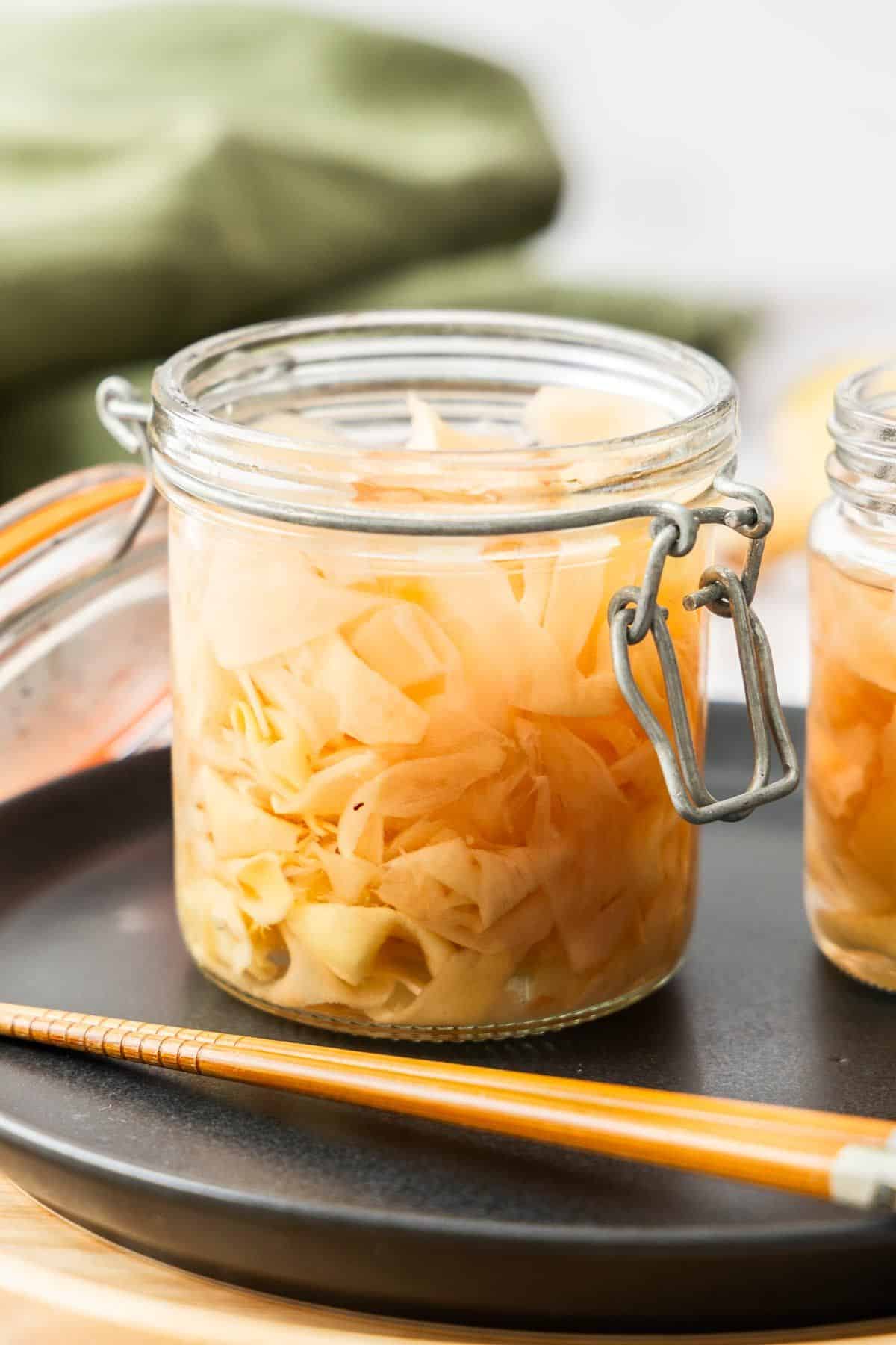 Jar of Pickled Ginger sitting on a black plate, with some chopsticks on edge of plate.