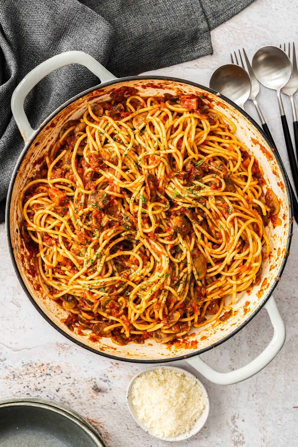 Mushroom and Tomato Pasta, garnished with finely chopped parsley, in a large skillet, some cutlery and cheese on the edge.