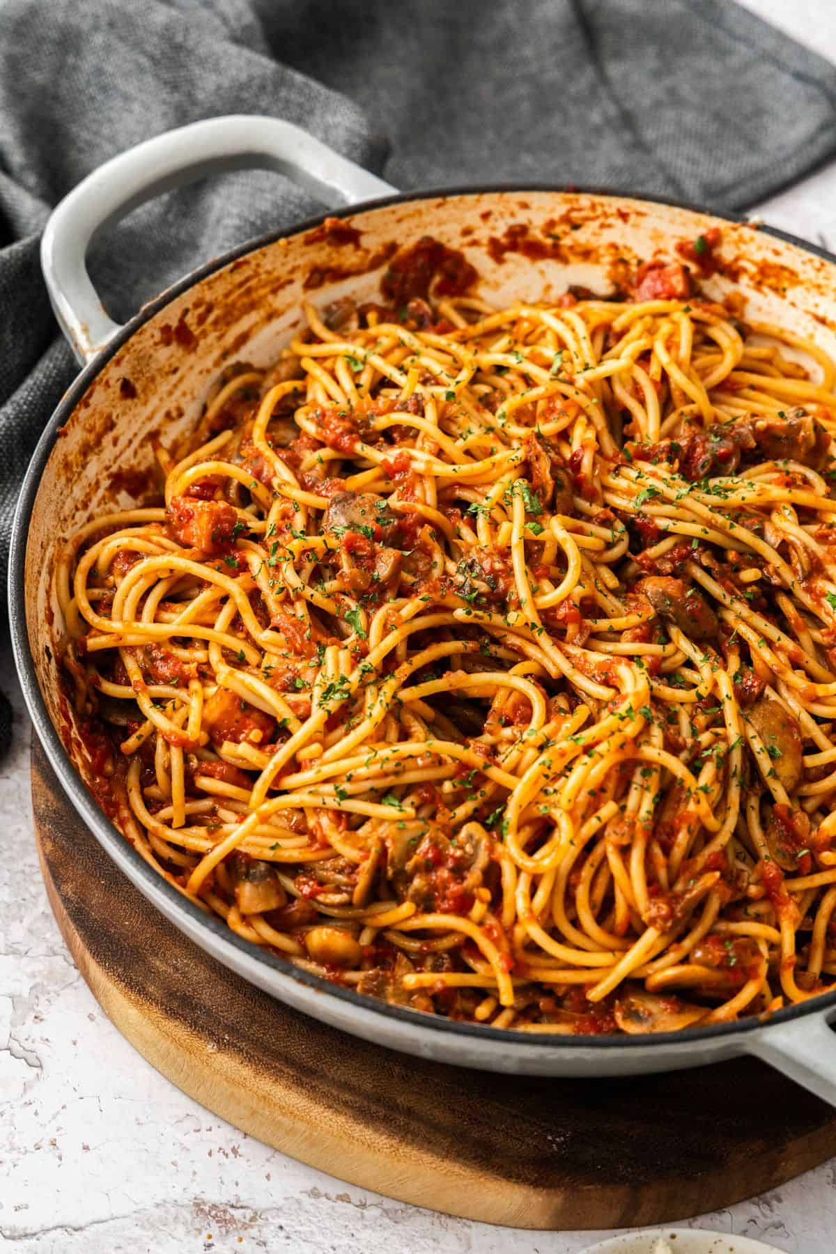 Mushroom and Tomato Pasta, garnished with finely chopped parsley, in a large skillet, sitting on a wooden board.
