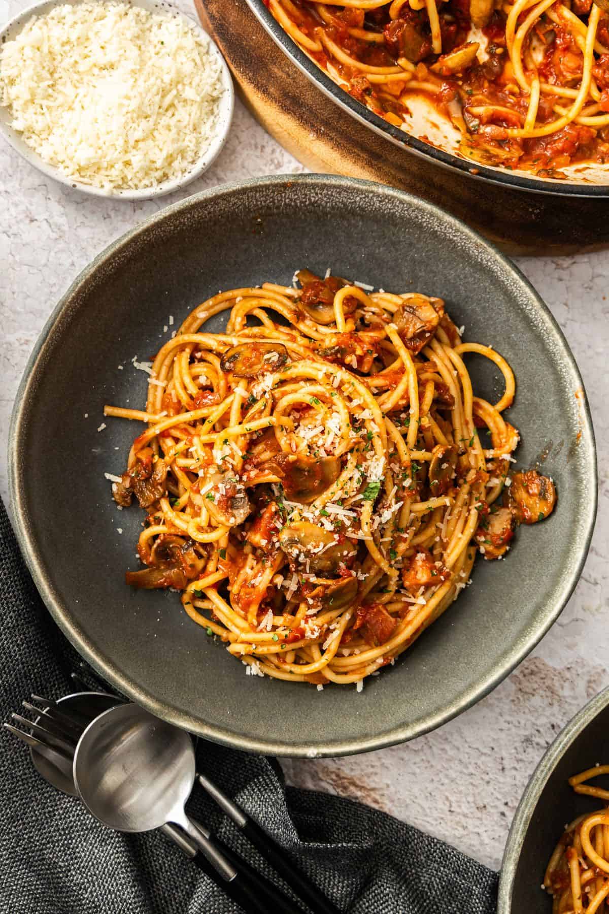 Round grey bowl of Mushroom and Tomato Pasta, garnished with some grated Parmesan cheese.