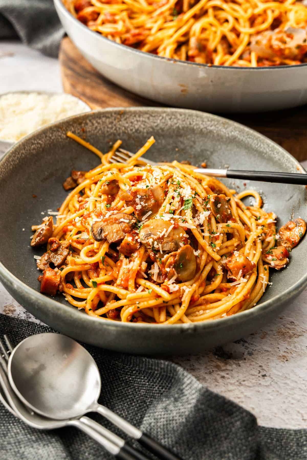 Round grey bowl of Mushroom and Tomato Pasta, garnished with some grated Parmesan cheese, a fork sitting in the bowl.