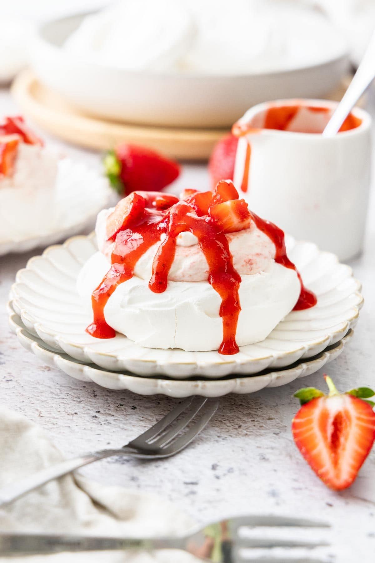 Plate with a meringue nest topped with strawberry whipped cream and strawberry sauce.