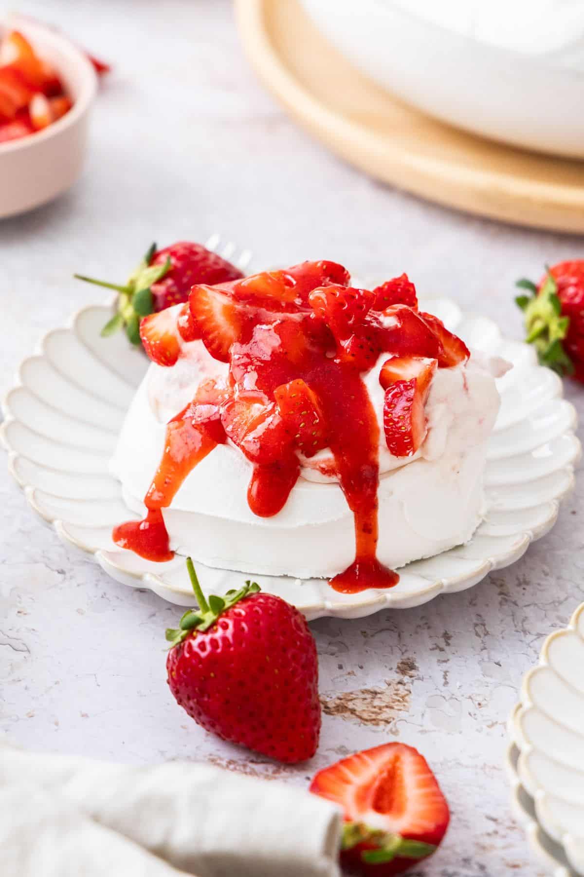 Plate with a meringue nest topped with strawberry whipped cream and strawberry sauce, some whole strawberries on edge.