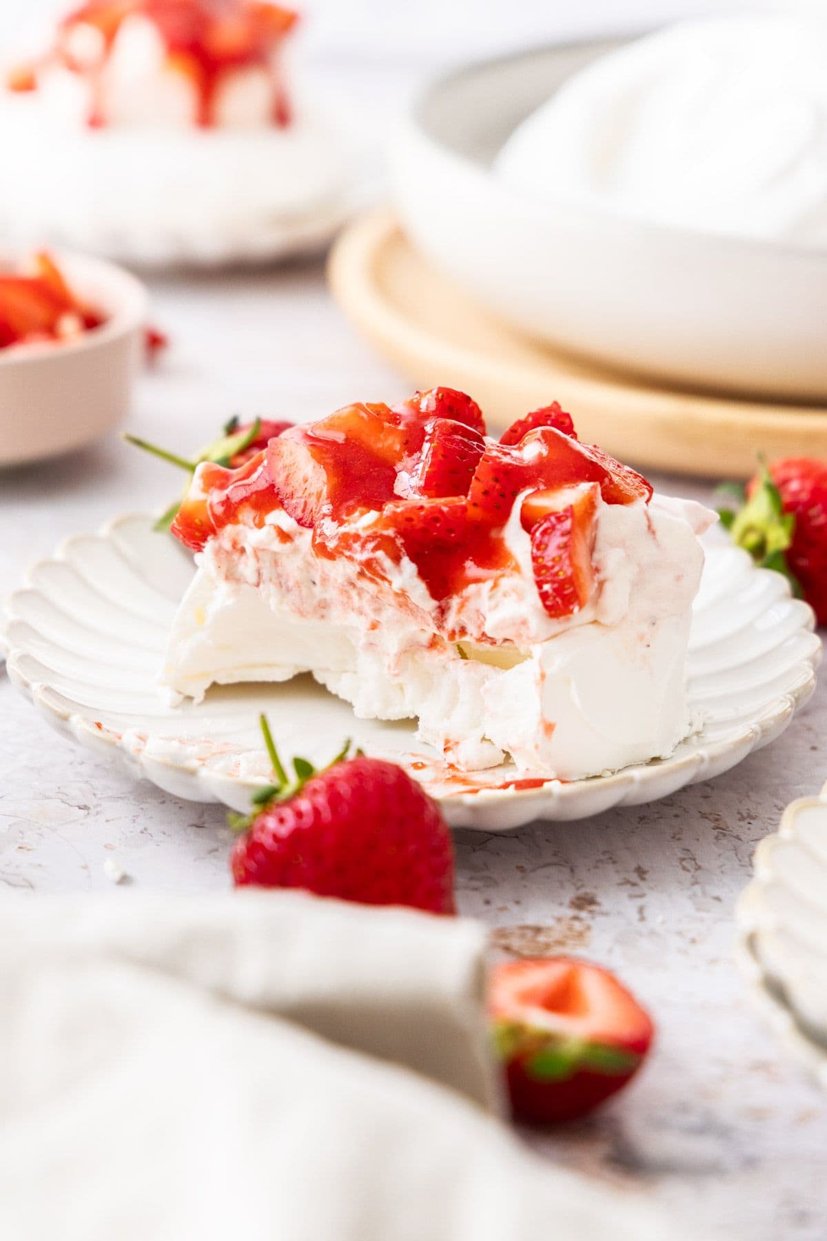 Plate with a meringue nest topped with strawberry whipped cream and strawberry sauce, with some of it having been eaten.