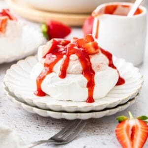 Plate with a meringue nest topped with strawberry whipped cream and strawberry sauce.