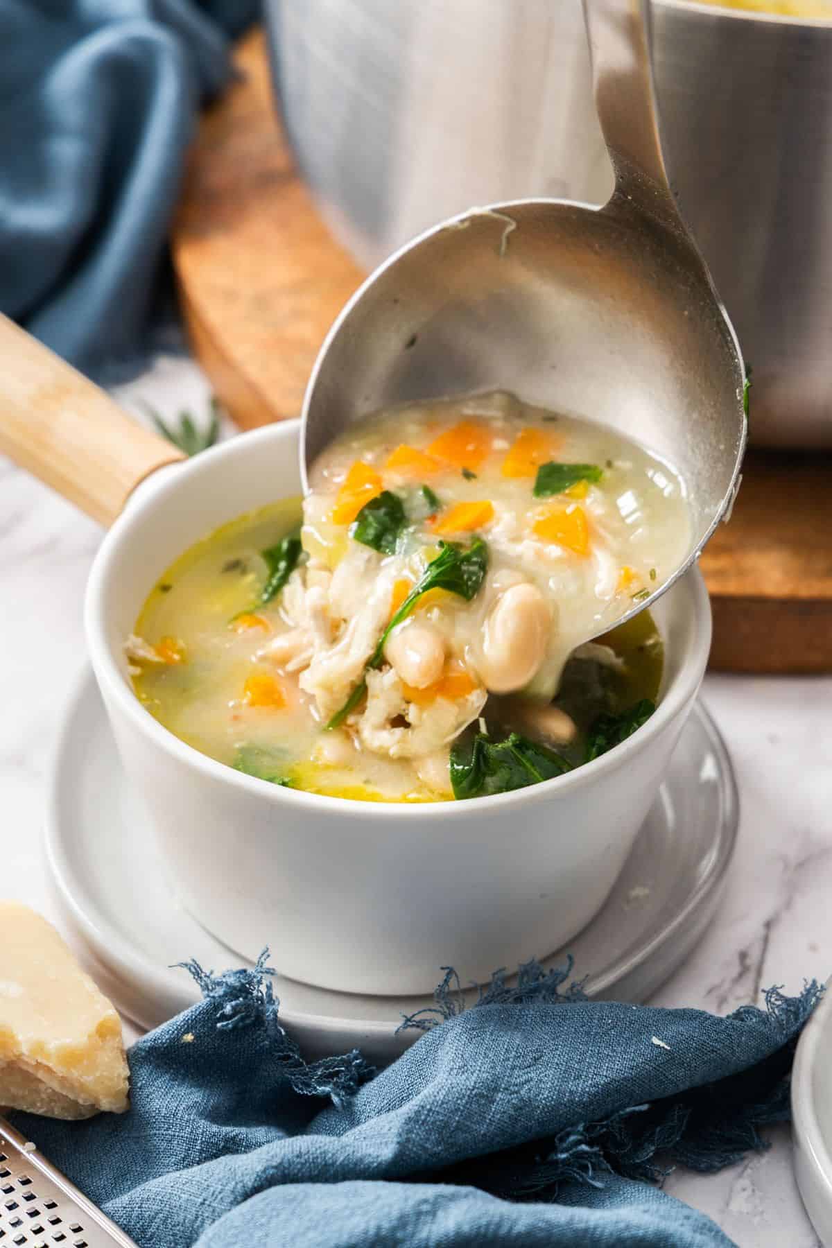 Soup ladle serving some soup into a small white bowl.