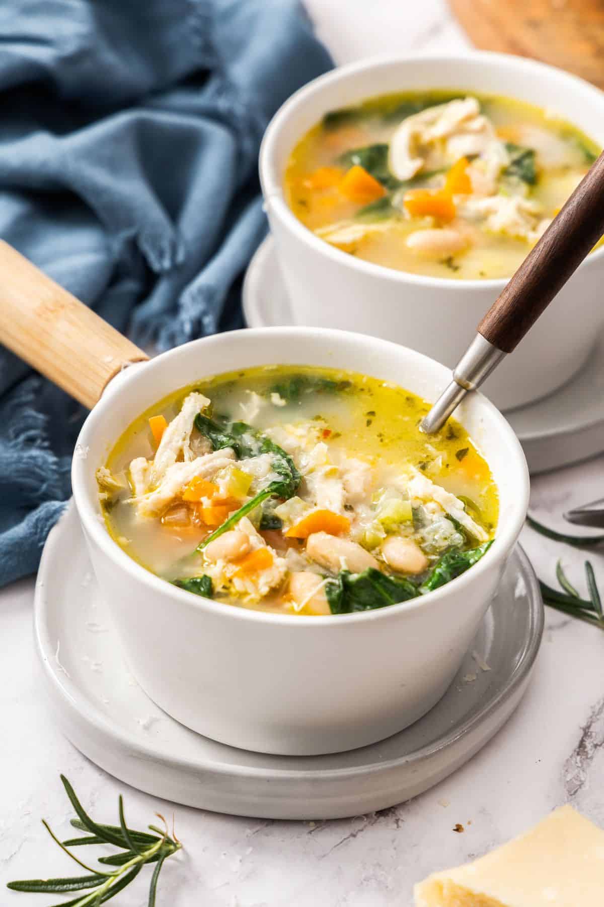Small white bowl of Chicken and White Bean Soup with a spoon resting in the bowl.