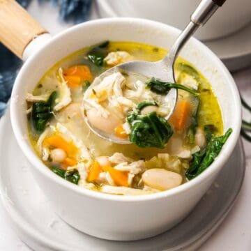 Small white bowl of Chicken and White Bean Soup with a spoon lifting up some soup.