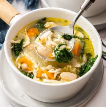Small white bowl of Chicken and White Bean Soup with a spoon lifting up some soup.