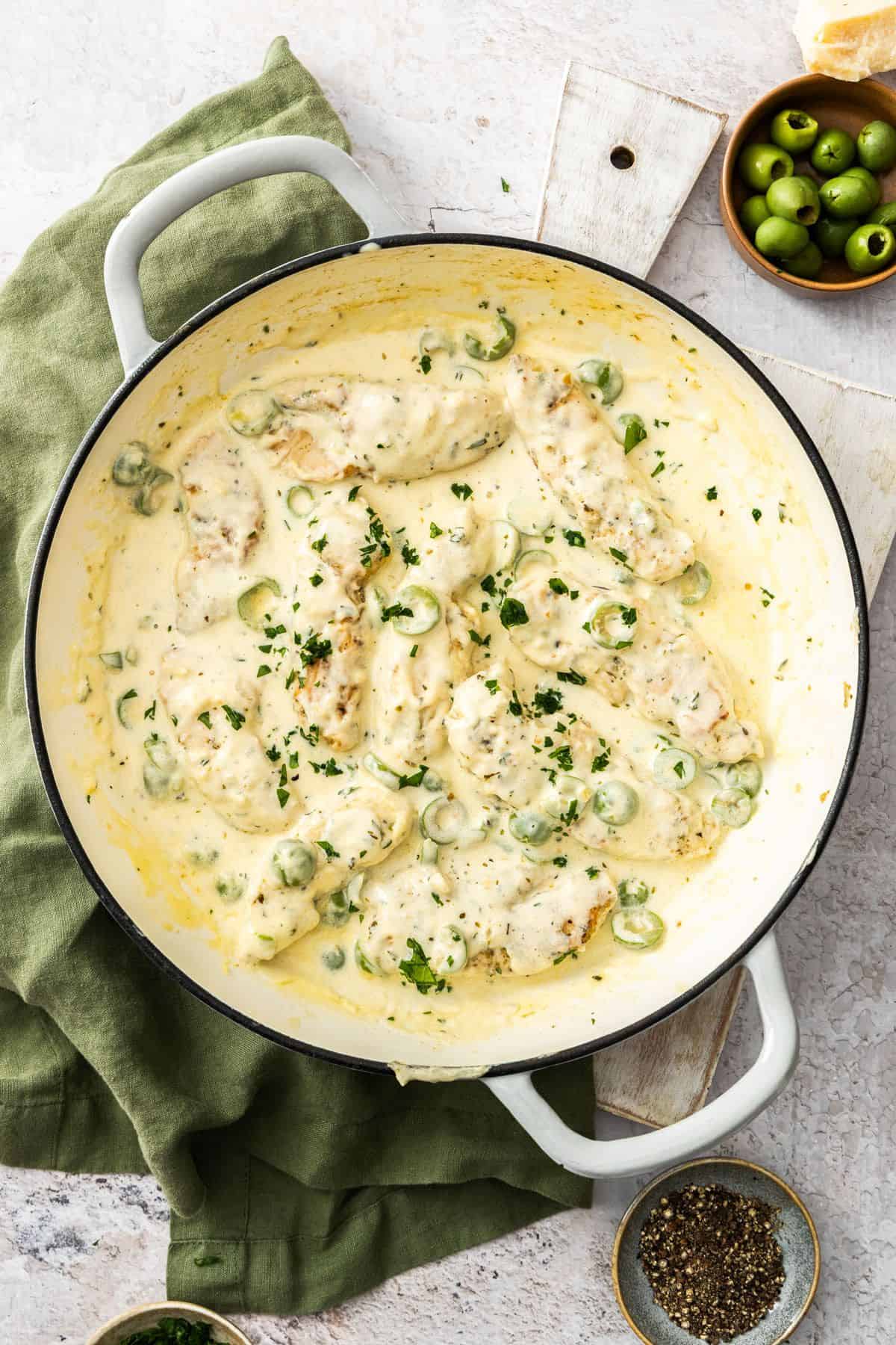 Round white skillet sitting on a green cloth, containing Creamy Garlic Chicken, garnished with a sprinkling of parsley.