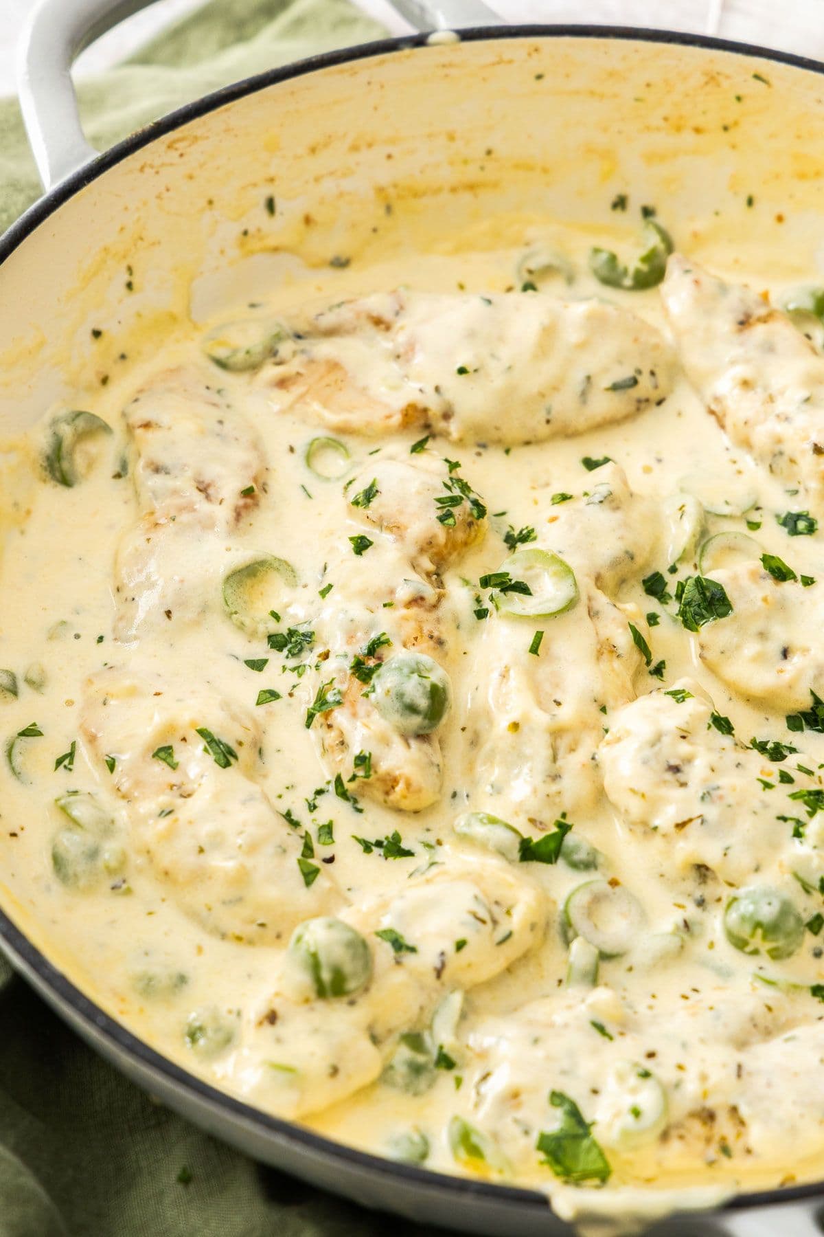 Round white skillet sitting on a green cloth, containing Creamy Garlic Chicken, garnished with a sprinkling of parsley.