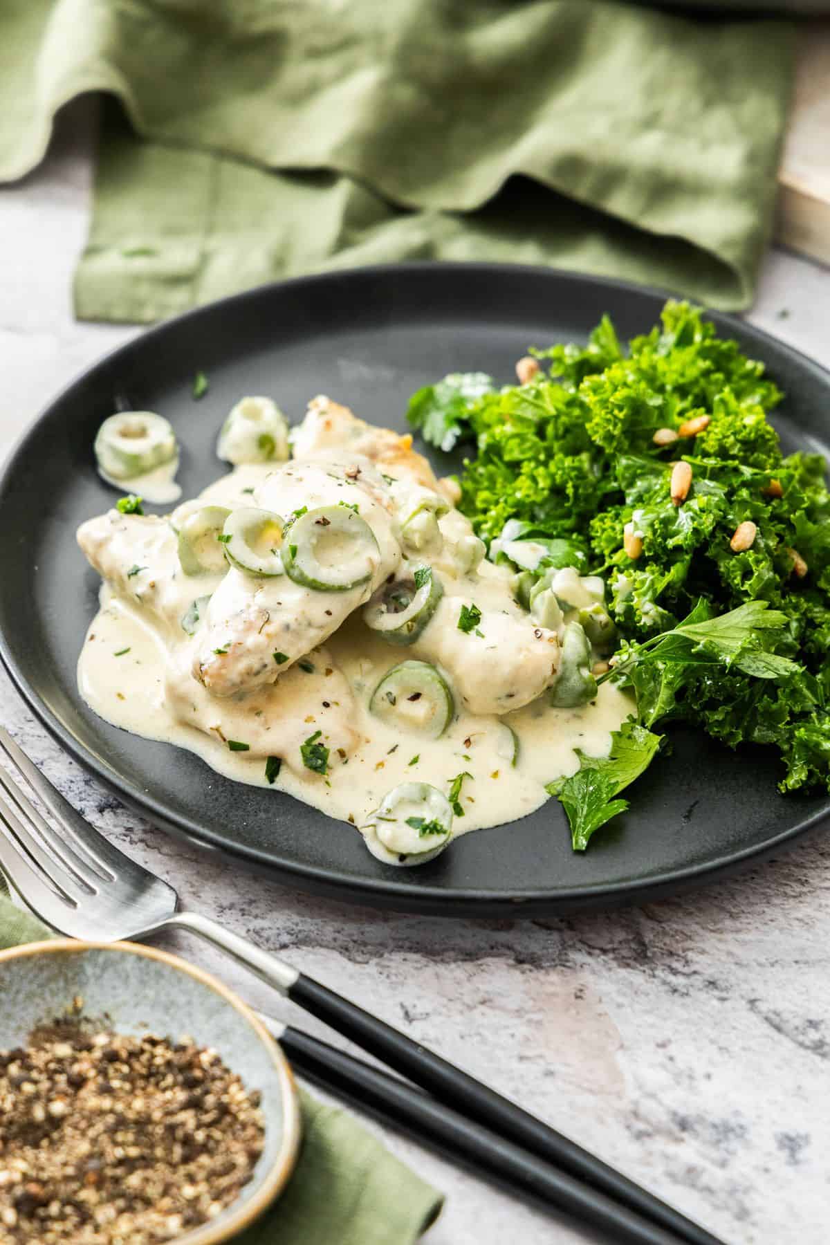 Round black plate with a serve of Creamy Garlic Chicken and a chopped kale salad on the side.