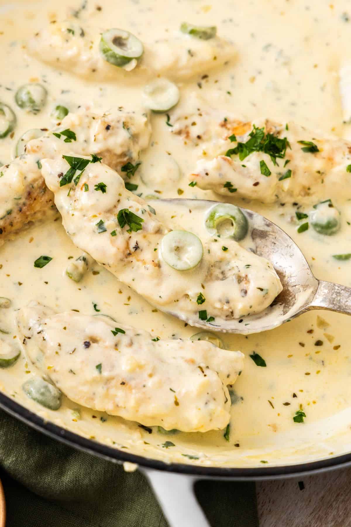Round white skillet containing Creamy Garlic Chicken, with a spoon lifting up a piece of chicken.