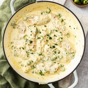 Round white skillet sitting on a green cloth, containing Creamy Garlic Chicken, garnished with a sprinkling of parsley.