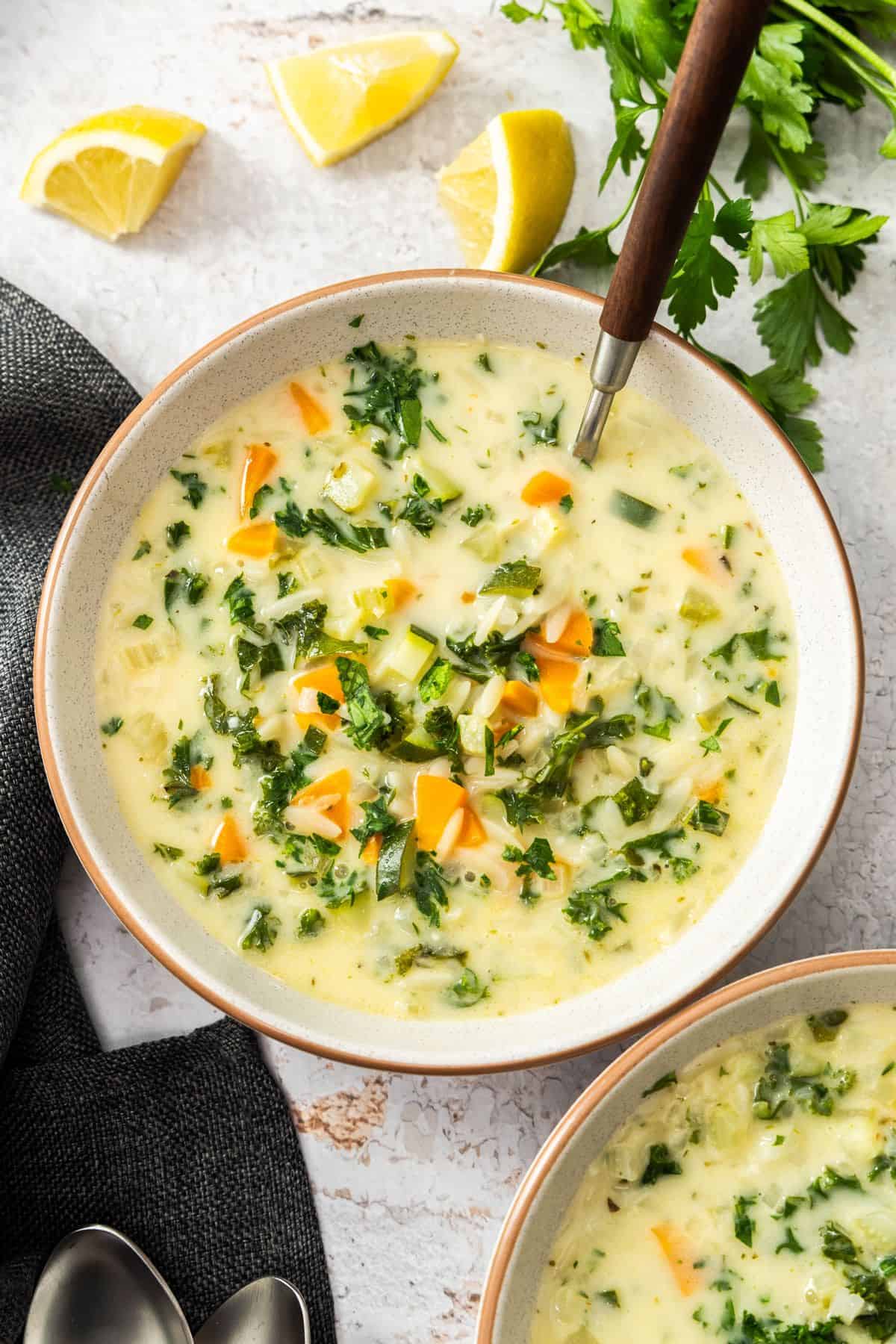 Round grey bowl with a serving of Creamy Orzo Vegetable Soup, with a spoon resting in the bowl.