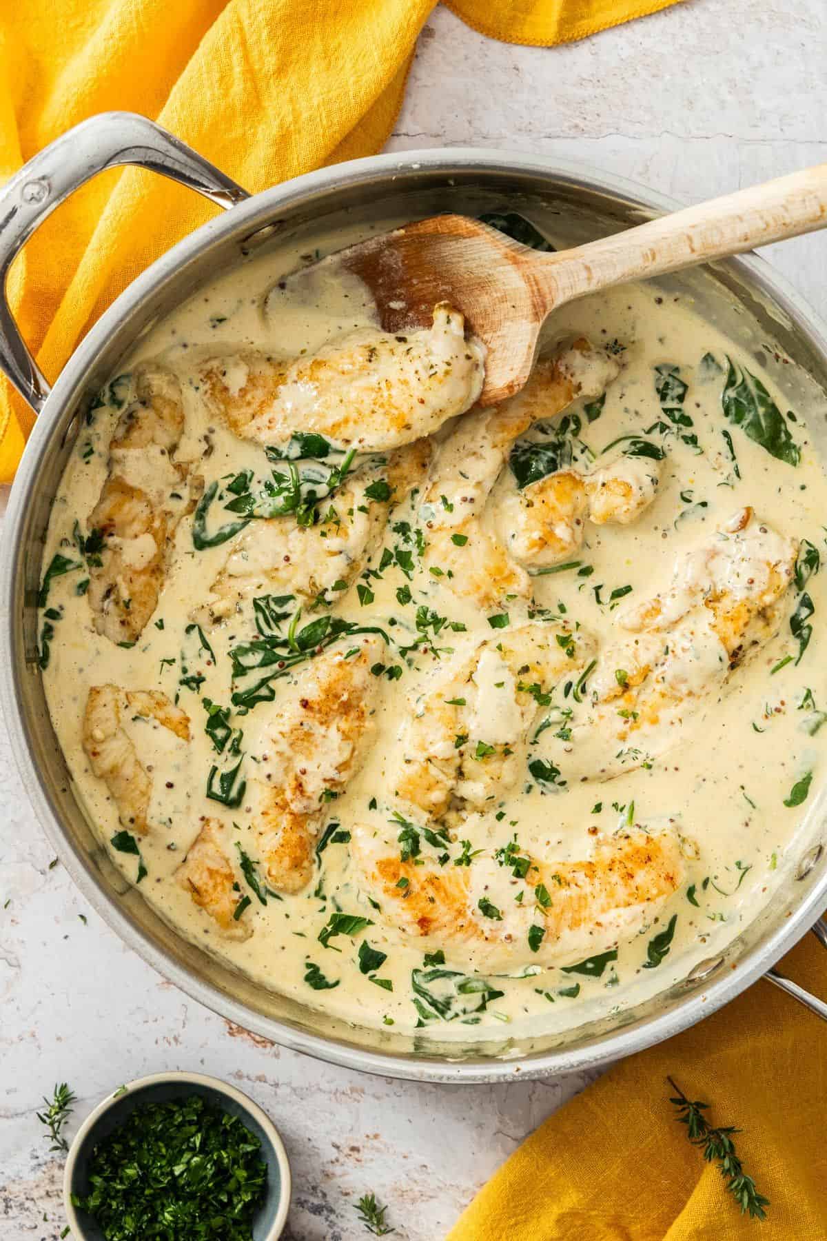 Large frying pan with Creamy Mustard and Spinach Chicken, with a wooden spoon resting in the pan.