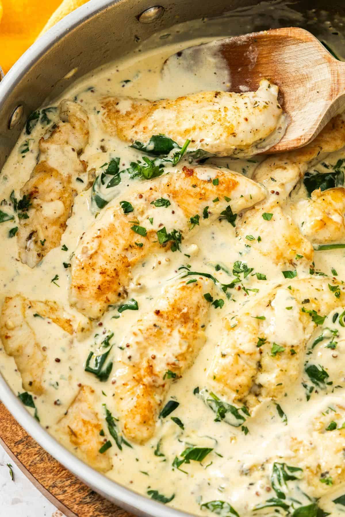 Large frying pan with Creamy Mustard and Spinach Chicken, with a wooden spoon resting in the pan.