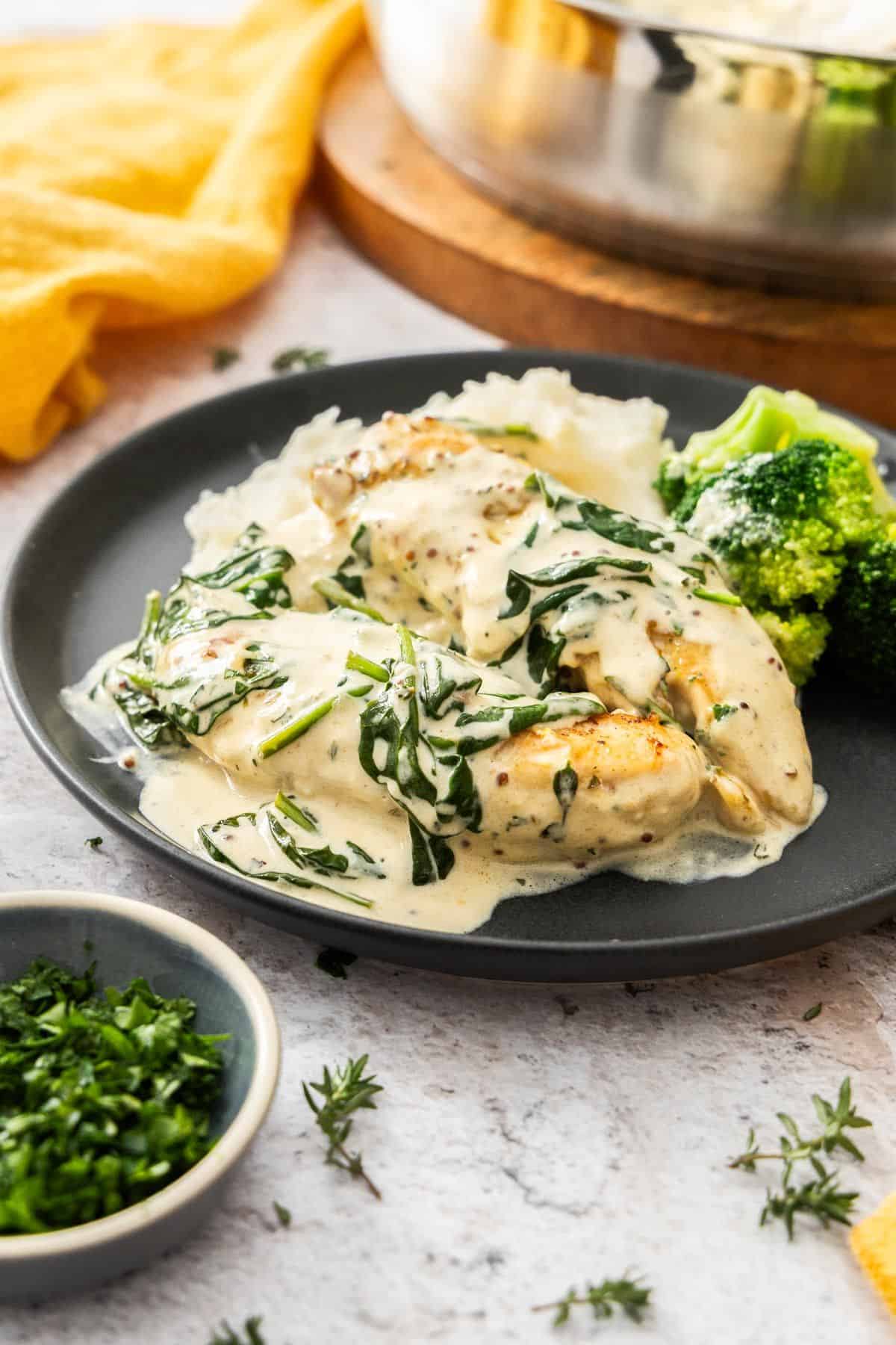 Serving of Creamy Mustard Chicken, alongside some broccoli and mashed potato, on a round black plate.