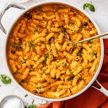 Large frying pan of Creamy Red Pepper Pasta, with a spoon resting in the pan.