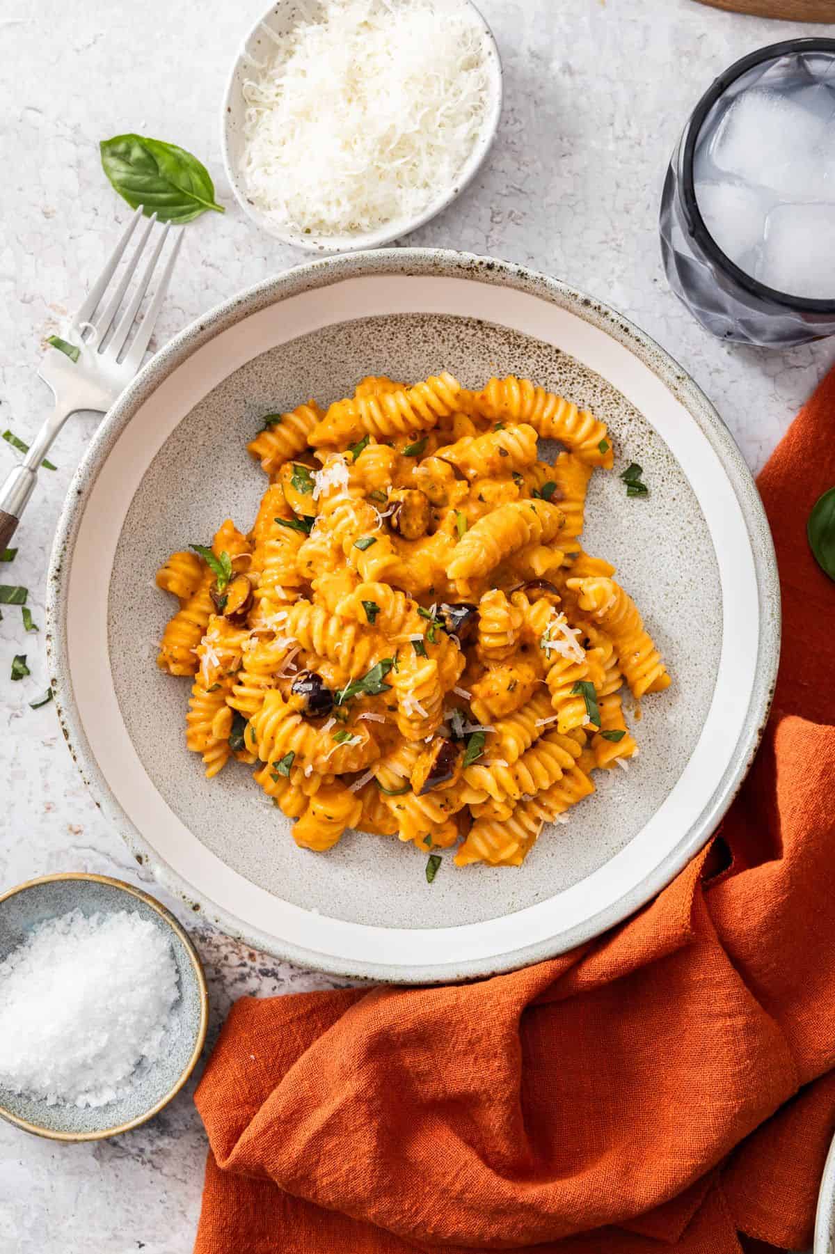 Round bowl with a serve of Roasted Red Pepper Pasta, garnished with fresh basil and Parmesan cheese.