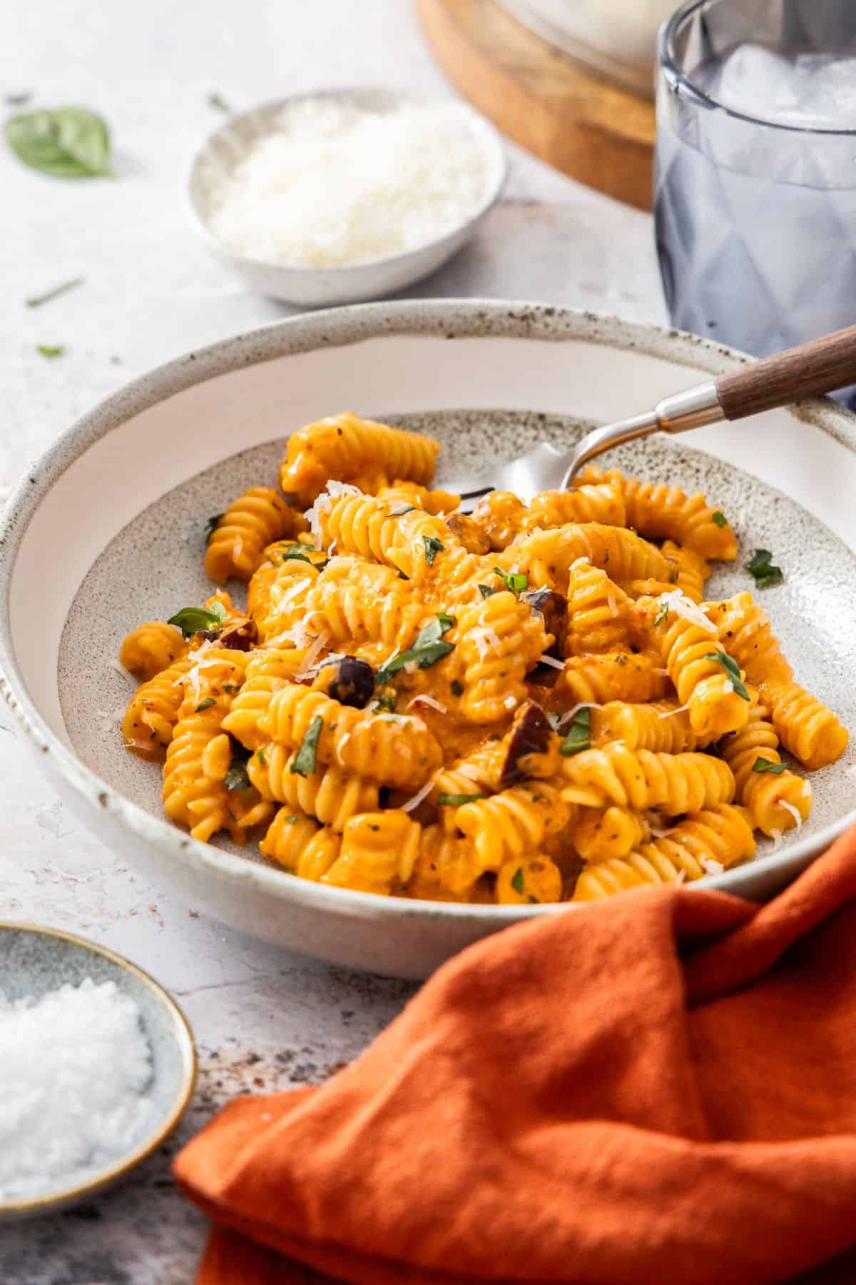 Round bowl with a serve of Roasted Red Pepper Pasta, garnished with fresh basil and Parmesan cheese, with a fork in the bowl.