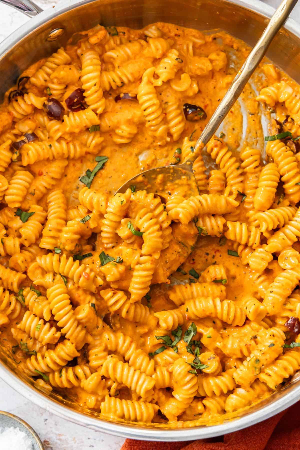 Large frying pan of Creamy Red Pepper Pasta, with a spoon resting in the pan.