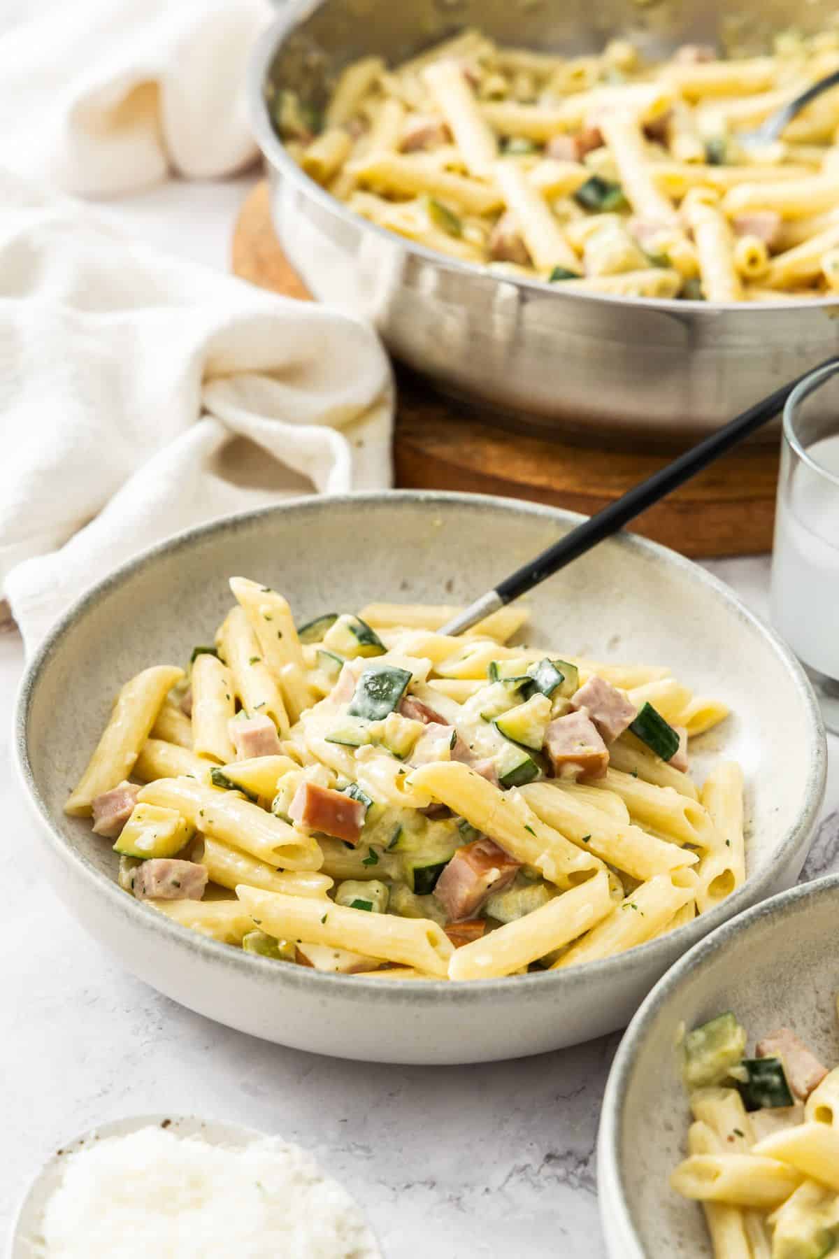 Round bowl with a serve of Creamy Zucchini Pasta with a fork resting in the bowl.