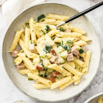 Round bowl with a serve of Creamy Zucchini Pasta with a fork resting in the bowl.