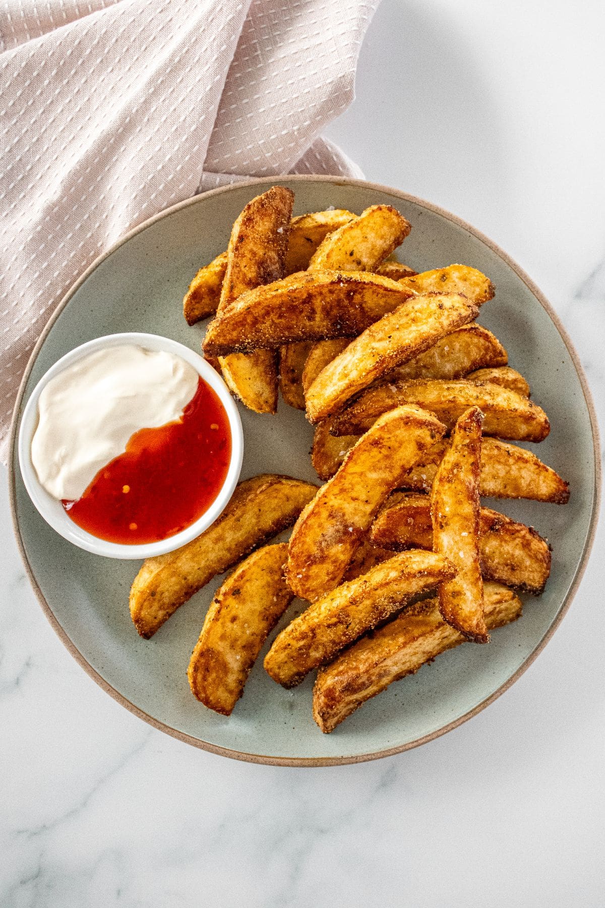 Round grey plate of Crispy Baked Potato Wedges, with a small dish of sour cream and sweet chilli sauce on the side.