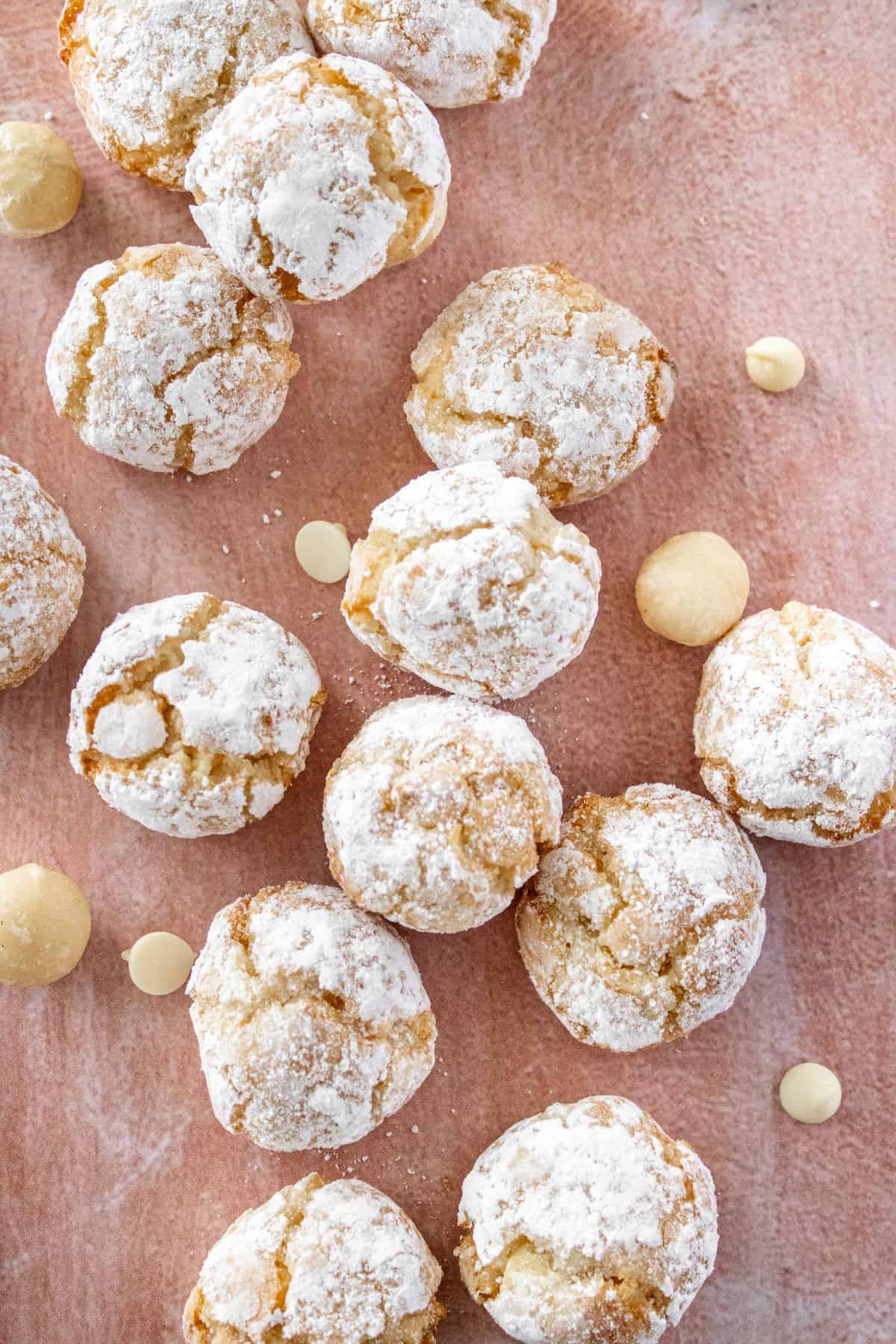 Gluten-Free Macadamia Cookies on a pink background with some white chocolate chips and macadamias around the edge.