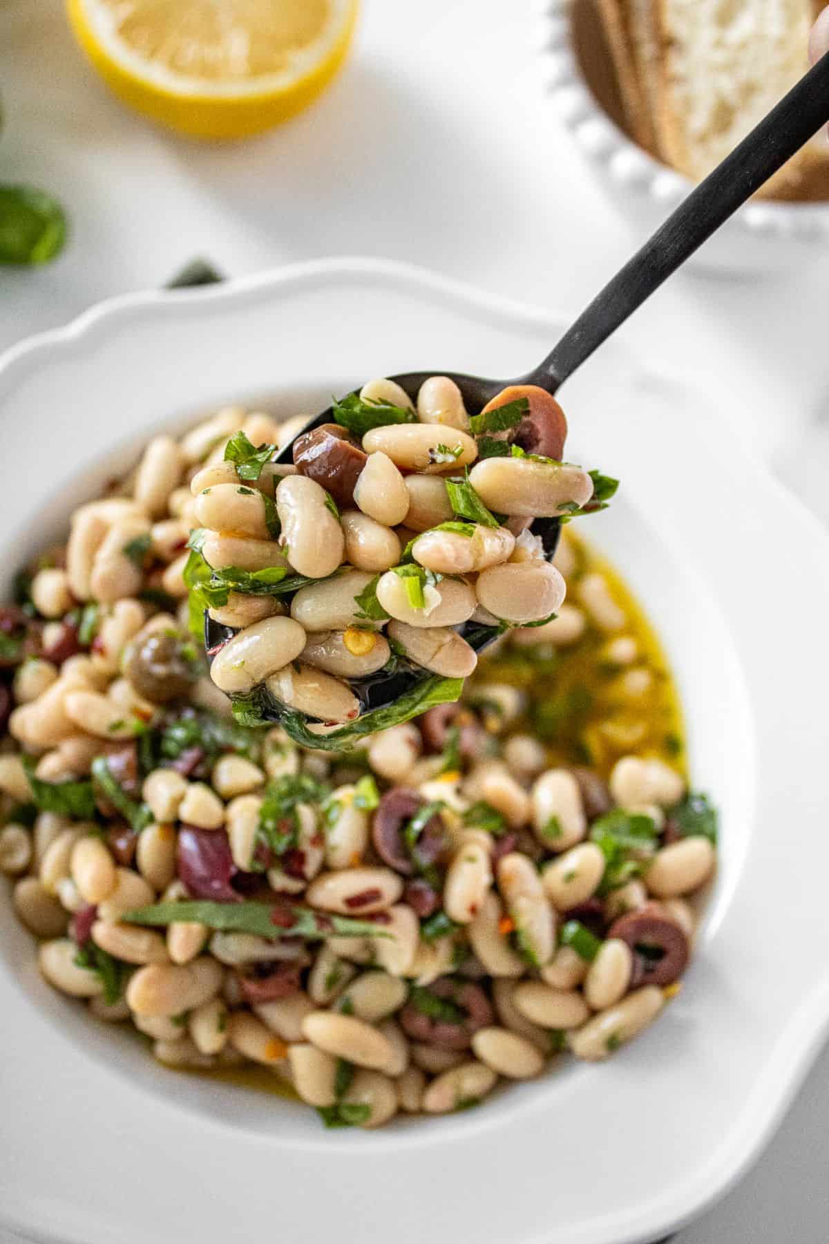 Spoon lifting up a serve of Marinated White Beans from a round white bowl.